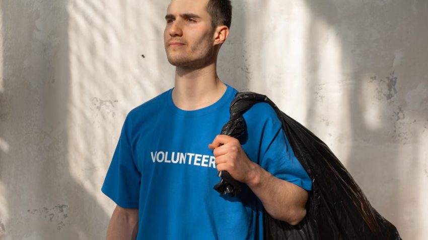 A young male volunteer holding a garbage bag indoors, promoting environmental protection.